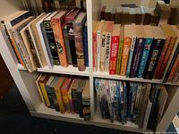 Two white bookcase shelves filled with assorted hardcover and paperback books