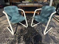 Front angled view of both chairs showing white tubular frames and teal upholstery