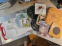 Group view showing plastic cutting board, baking sheet, tile coasters, cast iron trivets, wooden trivet and cutting board