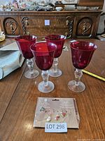 four ruby red goblets with clear stems and packaged wine charms on wooden table