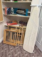Shelf showing iron, mat cutter box, quilting kit, embroidery hoops, frames, ironing board