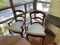 Two matching wooden French Provincial armchairs placed by windows