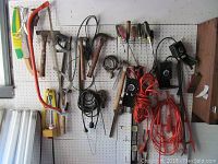 Wide view of assorted tools mounted on white pegboard, showing hammers, saws, screwdrivers, cords and other tools.