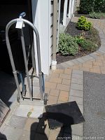 Metal hand truck with curved top handles and a metal base plate, showing signs of moderate wear placed outside a garage on a paved surface.