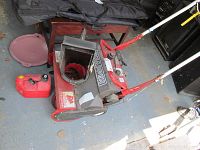 Side angle photo of red and black Snapper snowthrower with attached handles and visible label, small red gas can nearby