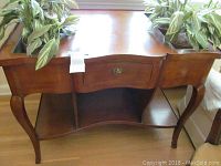 Wood planter table front view showing curved legs, small drawer with metal handle, lower shelf and planter compartments with artificial plants.