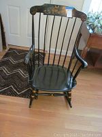 Full view of the black Boston style wooden rocking chair showing seat, armrests, and spindled back with curved top.