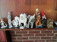Overview of nine assorted figurines on a shelf including angels, woman, elephant, clown, gnome, and bookends