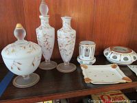 Overview of six Limoges porcelain decor items on wooden shelf showing various shapes and gold-pink floral painted accents
