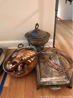 Photo showing tarnished silverplated warming dishes with lids and handles, copper bowl with utensils, and a rectangular warming dish with lid.