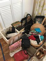 Overview of assorted handbags, purses, and a round woven basket grouped together on floor.
