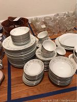 Wide view showing stacked plates, cups, saucers, and bowls with floral patterned English Garden china. Also visible in the background are some glassware items.