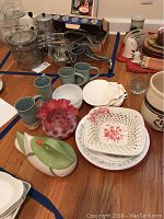 Full view of assorted kitchen and decorative items including mugs, dishes, ceramic duck figurine, shell dishes, and utensil holder on table.