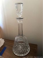 Tall Waterford crystal decanter with stopper on a wooden surface, diamond and star cut detailing visible.