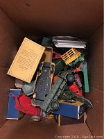 Photo shows a cardboard box filled with assorted Dinky toy vehicles and a stack of baseball cards.