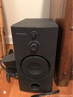 Front view of Harman Kardon black subwoofer speaker with volume and bass dial controls on front panel.