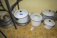 Wide shot of all cookware showing three pots with lids and multiple stacked metal baking pans and molds on yellow patterned floor.