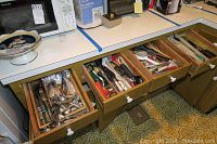 Open kitchen drawers showing a variety of utensils and kitchen tools arranged loosely in wooden compartments.