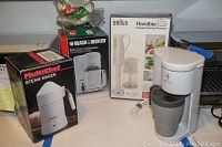 Photo showing packages and products including Multichef Steam Maker box, Black & Decker Brew n Go coffee maker box, Braun Hand blender box, and the actual steam maker unit.