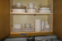 White Centura by Corning dishes arranged neatly on shelves including plates, bowls, cups, saucers, and glass bakeware.