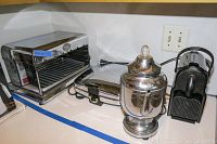 Shows the Nespresso Coffee Machine, Flec broiler, waffle maker, and coffee percolator on a countertop with power cords visible