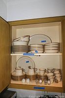 Full view of upper and lower cabinet shelves showing stacks of plates, bowls and cups
