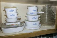 Stacked collection of white CorningWare dishes with blue cornflower pattern and clear Pyrex bowls on shelf.
