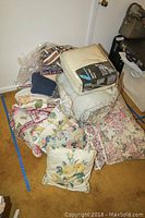 Pile of assorted comforters, pillows, and blankets with floral patterns and some items still in plastic packaging.
