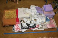 Overview of assorted folded bath towels, hand towels, pillowcases, sheets, and shower curtains on carpeted floor.