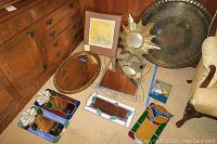 Overview of various wall decor items including mirrors, brass tray wall art, and stained glass pieces laid on the floor by wooden dresser.