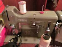 Close-up of olive green Necchi sewing machine mounted in wooden table with spools on top