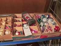 Top view photo showing multiple cardboard divider boxes containing assorted vintage glass Christmas balls with various colors and painted indent patterns.
