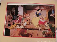 Framed colorful Disney lithograph depicting Snow White with the Seven Dwarves in a cabin