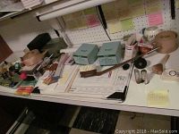 Wide view of basement workspace showing various office items and packing materials on white desk with pegboard wall behind.