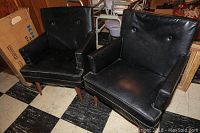 Pair of black vinyl mid century modern armchairs with wooden tapered spindle legs, showing button tufted backs and squared arms.