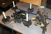 Photo showing two iron items laid on a table: a wall mount bell with four brass bells, curved iron structure and a four-candle electric chandelier with white candle-like bulbs.