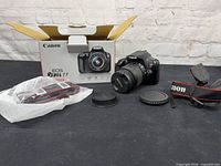 Camera body with attached 18-55mm lens, lens caps, strap, and box displayed on table