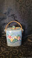 Front view of blue ceramic biscuit barrel with fruit relief and wicker handle