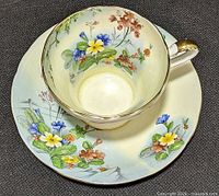 Top view of cup resting on saucer showing floral pattern, colouring and gilt trim