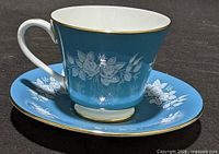 Side view of teacup on saucer showing color, floral motif and gold trim