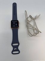 Watch face powered on showing pairing screen beside navy band and charging cable