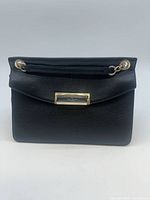 Front view of black pebbled leather shoulder bag showing gold logo plate and chain strap attachments