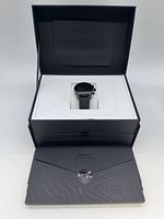 Box opened showing smartwatch seated, envelope with manuals below