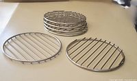 Six round stainless steel wire grates shown: two laid flat, four stacked