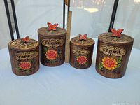 Four canisters upright with lids and ruler for scale