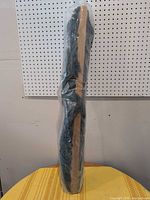 Hammock wrapped in plastic standing vertically against pegboard, wood spreader bar visible