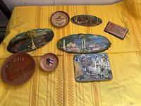 Group shot of all eight souvenir wood plaques and dishes on yellow cloth