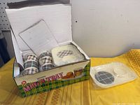 Opened box showing six plaid mugs and stack of matching cream trays