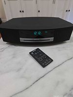 Front view of Bose Wave Music System with remote on marble surface, display lit 12:12
