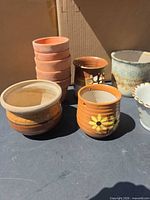 Group of pots showing stacked terracotta pots, banded pot, orange flower pot, brown/white cut-out pot, patina pot